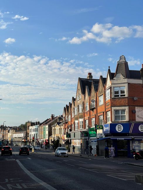 The image depicts a cylindrical public landmark structure located on a street corner in Gipsy Hill, East Ham, with a domed top and a sign reading 'EAST HAM'. The structure is black with graffiti tags