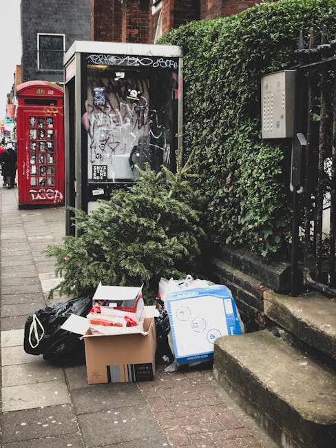 A large pile of discarded household items and waste on a pavement, including broken and intact ceramic plates, bowls, cups, and glassware, along with cardboard boxes, plastic packaging, and miscellaneous debris. Some items appear shattered with broken edges and fragments scattered throughout. The background shows a mix of kitchenware and refuse, indicative of waste removal or clearance. This scene reflects the disposal process involved in house removals, such as clearing out household contents before relocation, with a focus on bulky waste management. The image emphasizes the importance of proper waste disposal in house moving services provided by Man with Van Gipsy Hill, supporting efficient and responsible household item removal in SE19.