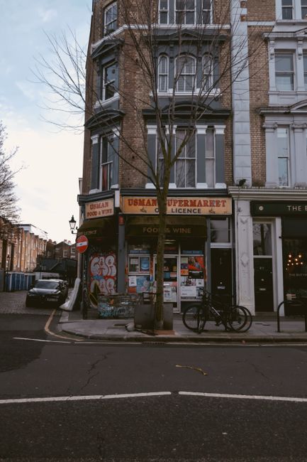 A street scene in Gipsy Hill showing a corner building with a ground-floor coffee shop, featuring large windows and a black sign displaying 'COFFEE' in white lettering. Outside the shop, a person is s